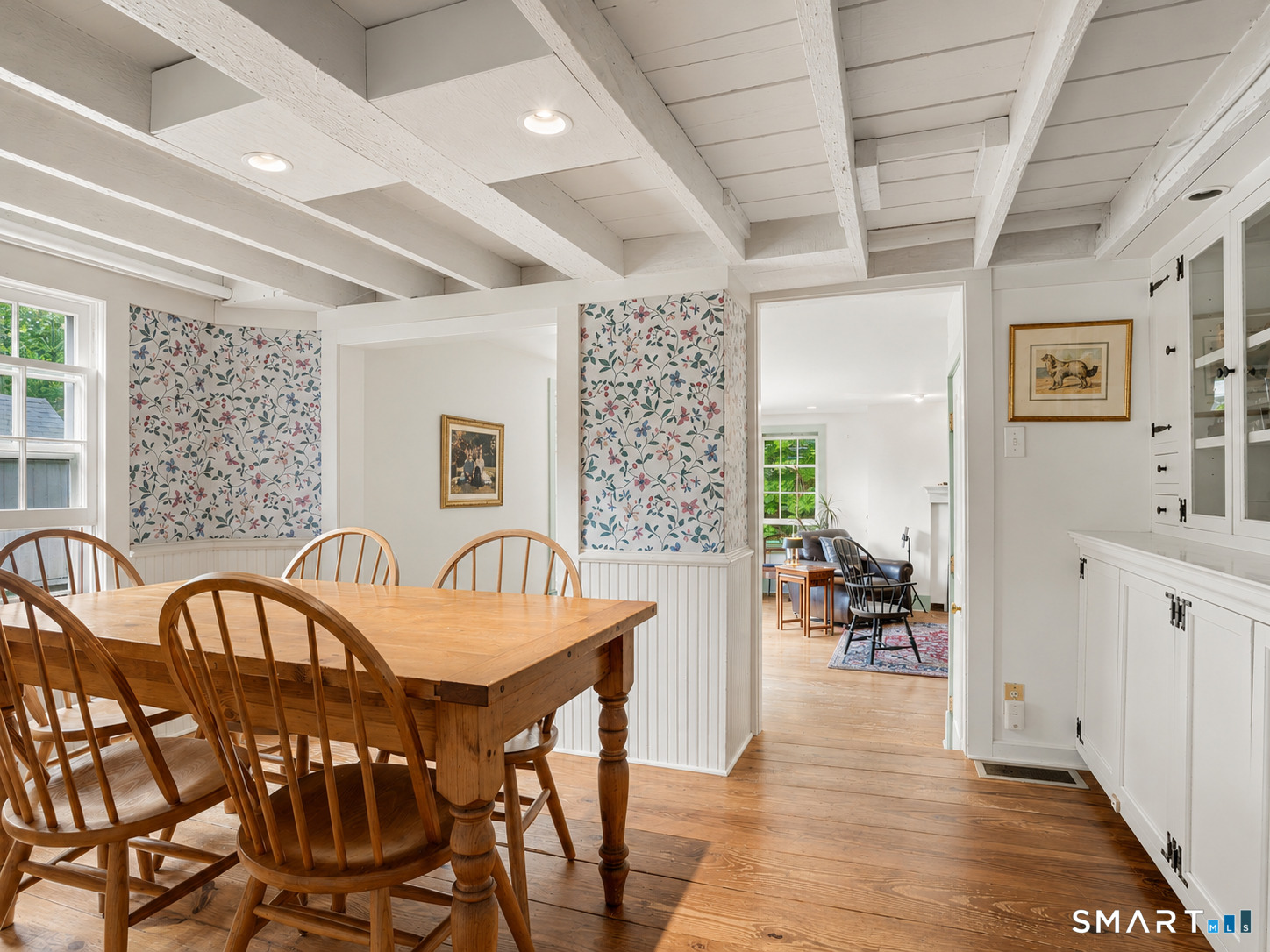 Dining room with a wooden table, floral shades, white built-ins, and exposed ceiling beams.
