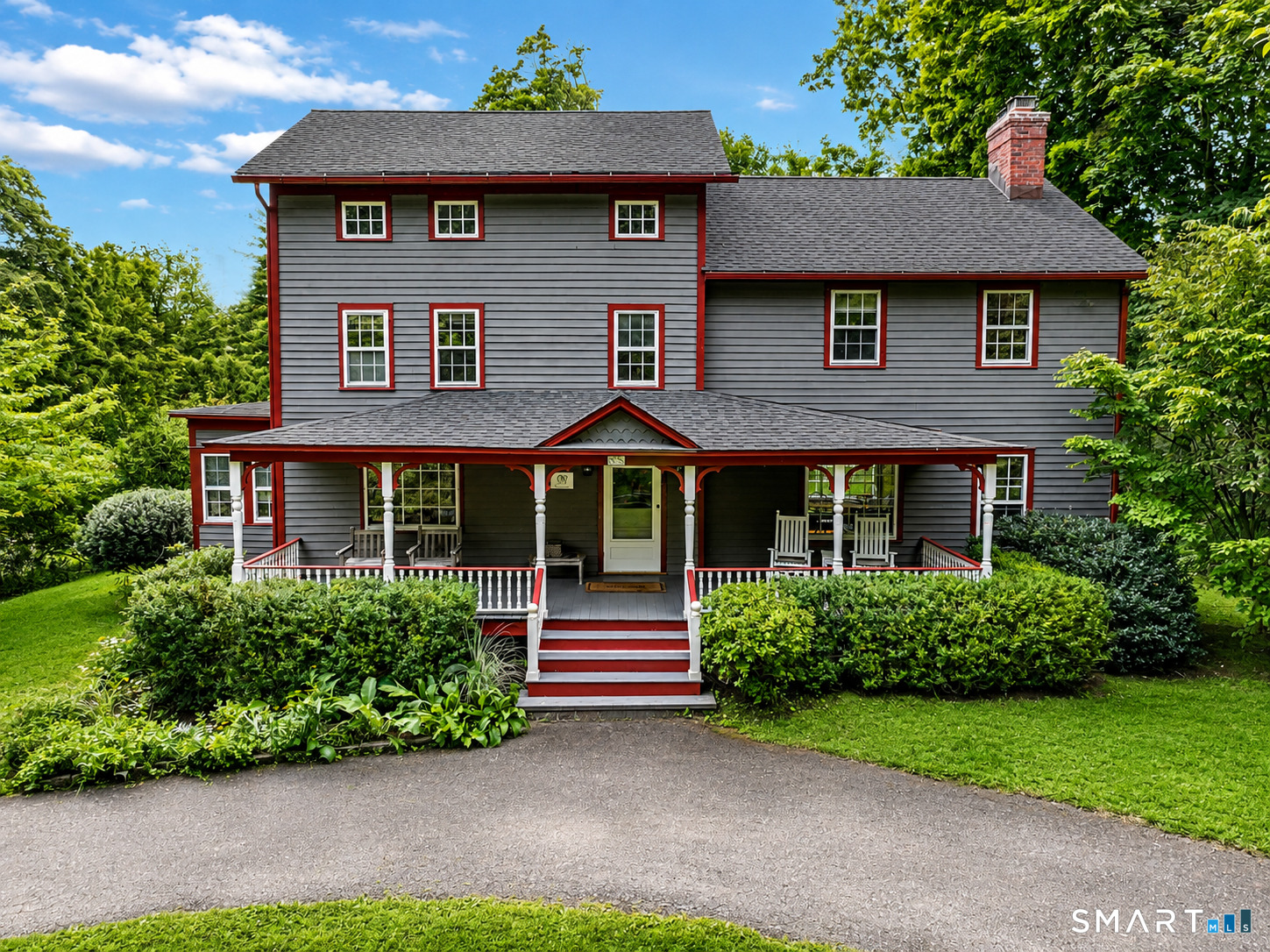 Gray two-story house with red trim, a broad covered porch, and landscaped front yard.