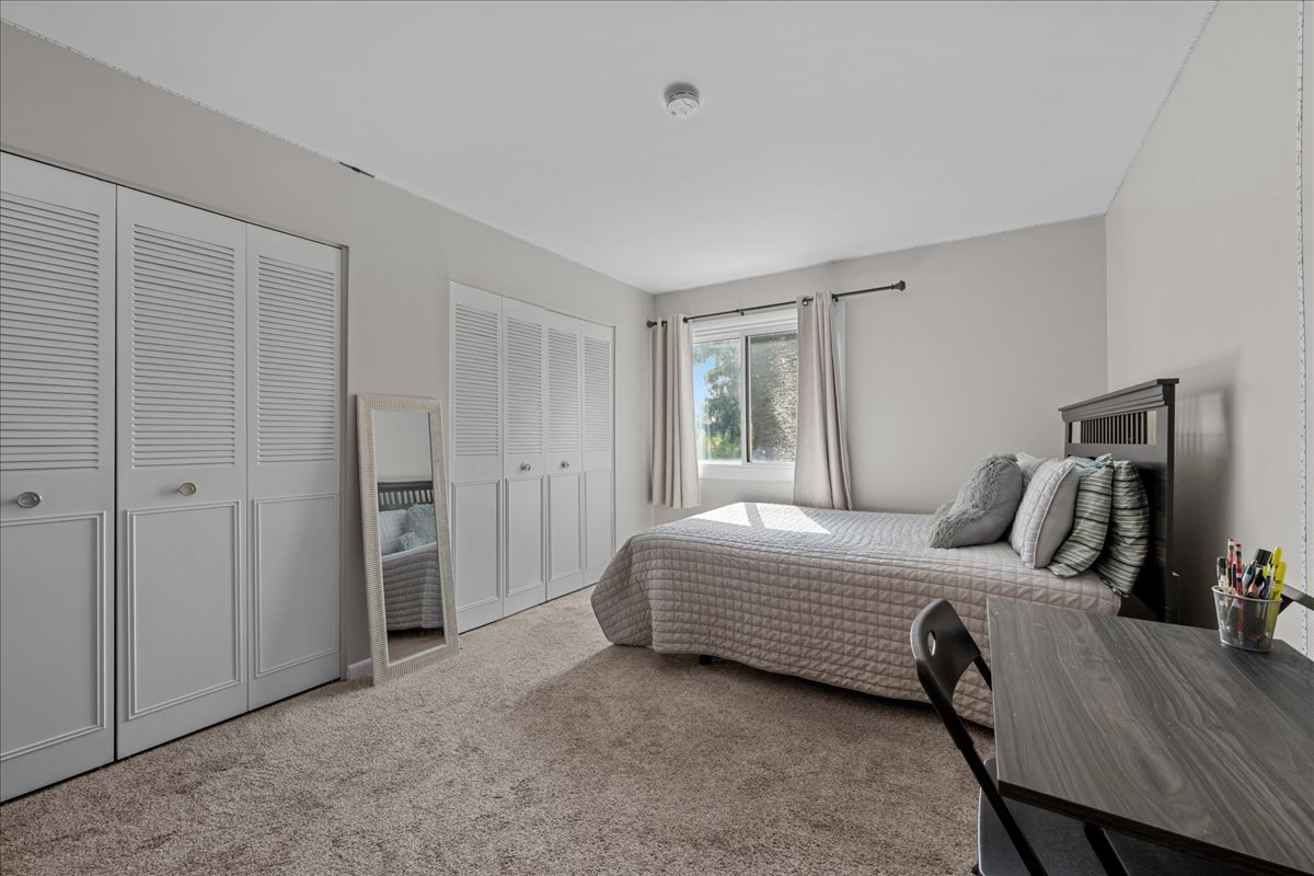 Bedroom with a gray quilted bed, built-in white closets, and a desk by the window.
