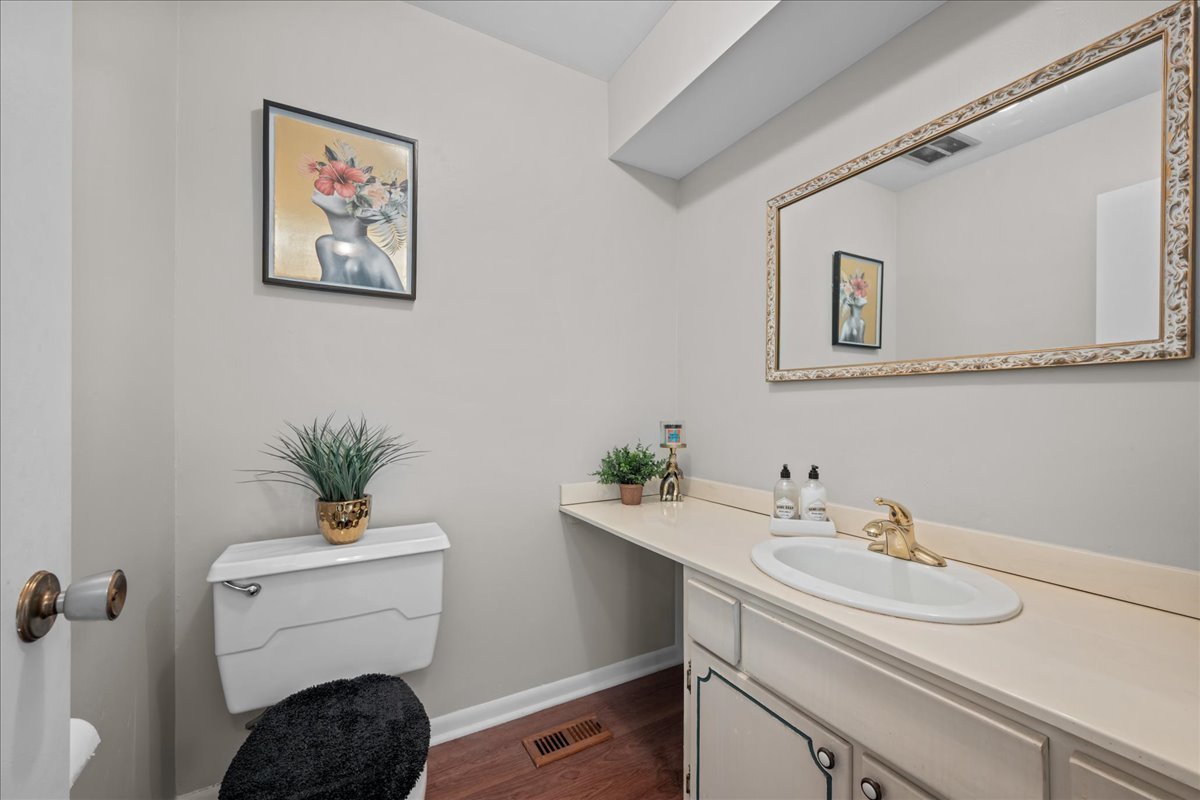 Powder room with a white vanity, ornate mirror, and toilet beneath floral artwork.