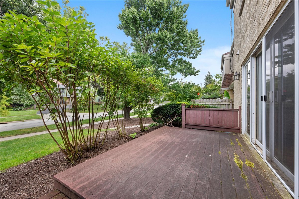 Raised deck beside the home, bordered by leafy shrubs and a low wooden railing.