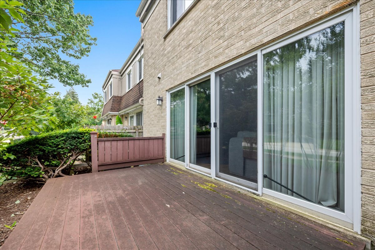 Wooden deck beside a tan brick townhouse, with sliding glass doors and a privacy railing.