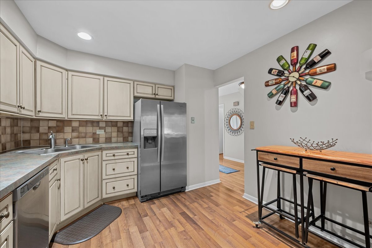 Kitchen with cream cabinets, stainless appliances, a tiled backsplash, and wood-look flooring.