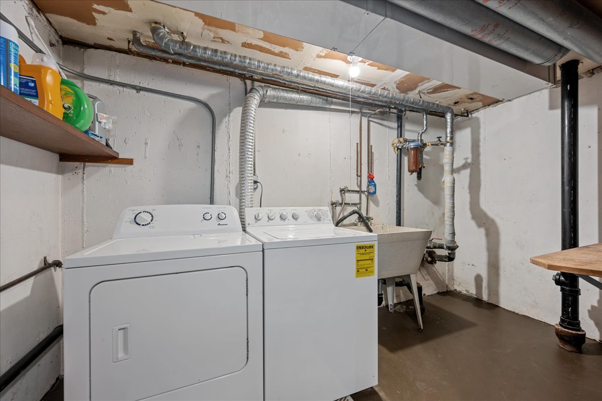 Basement laundry area with a white washer and dryer beside a deep utility sink and exposed ductwork.