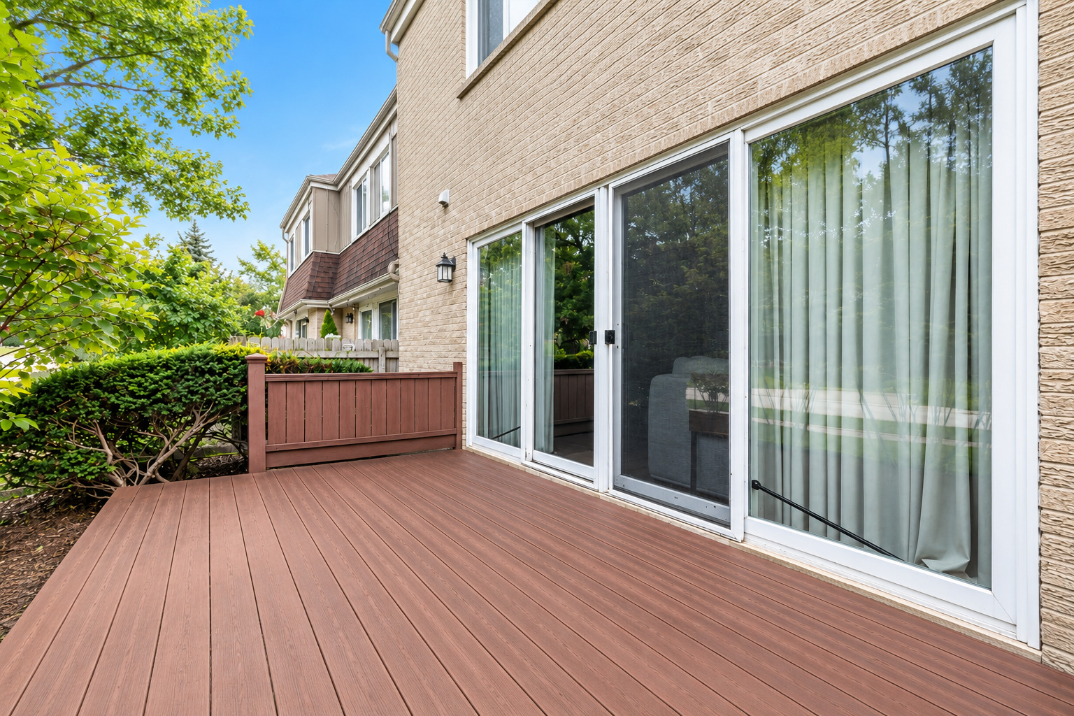 Spacious composite deck beside a tan-sided home, with sliding glass doors and a wood privacy railing.