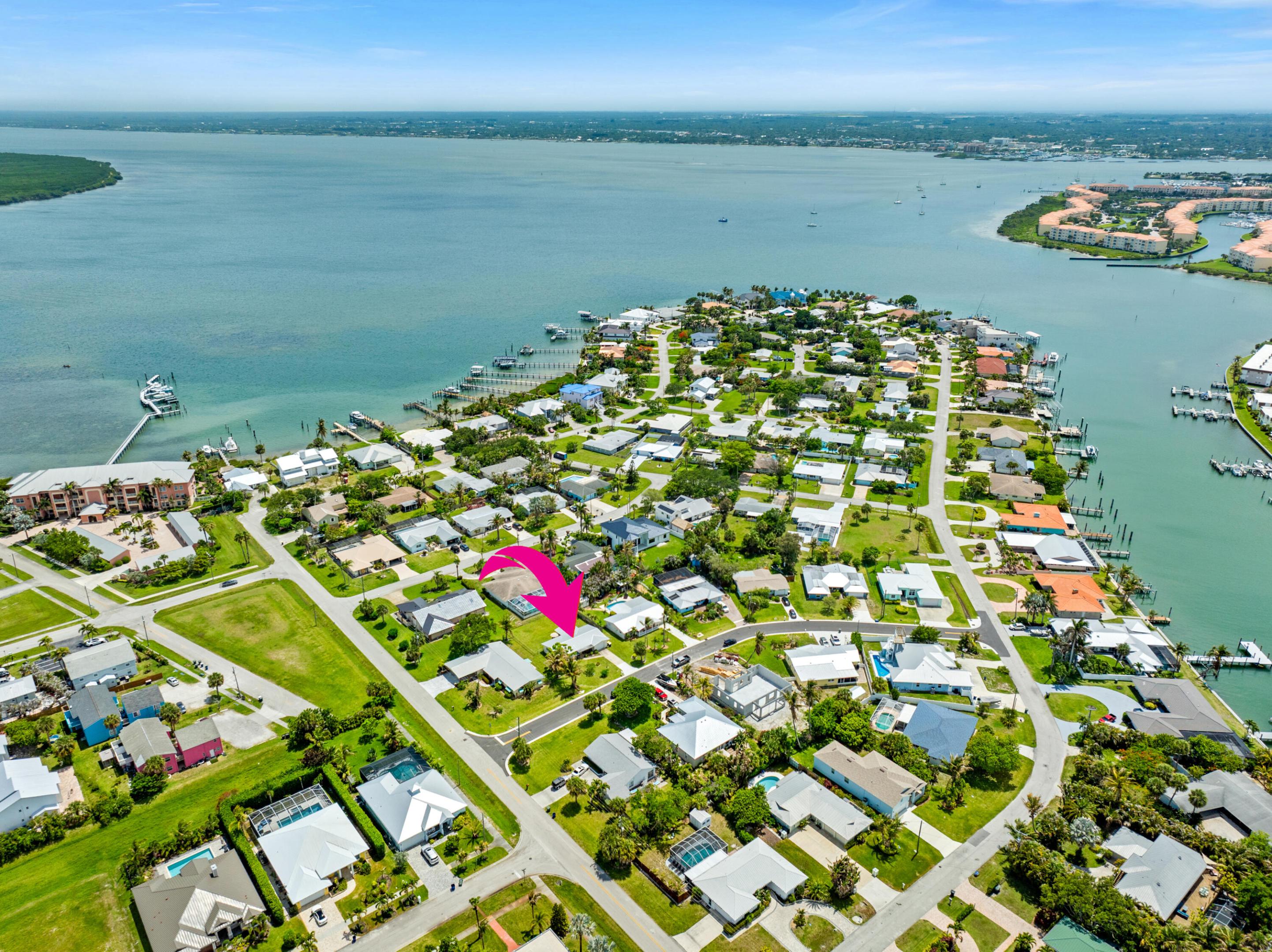 Aerial view of waterfront homes and docks, with a pink arrow pointing to one house.