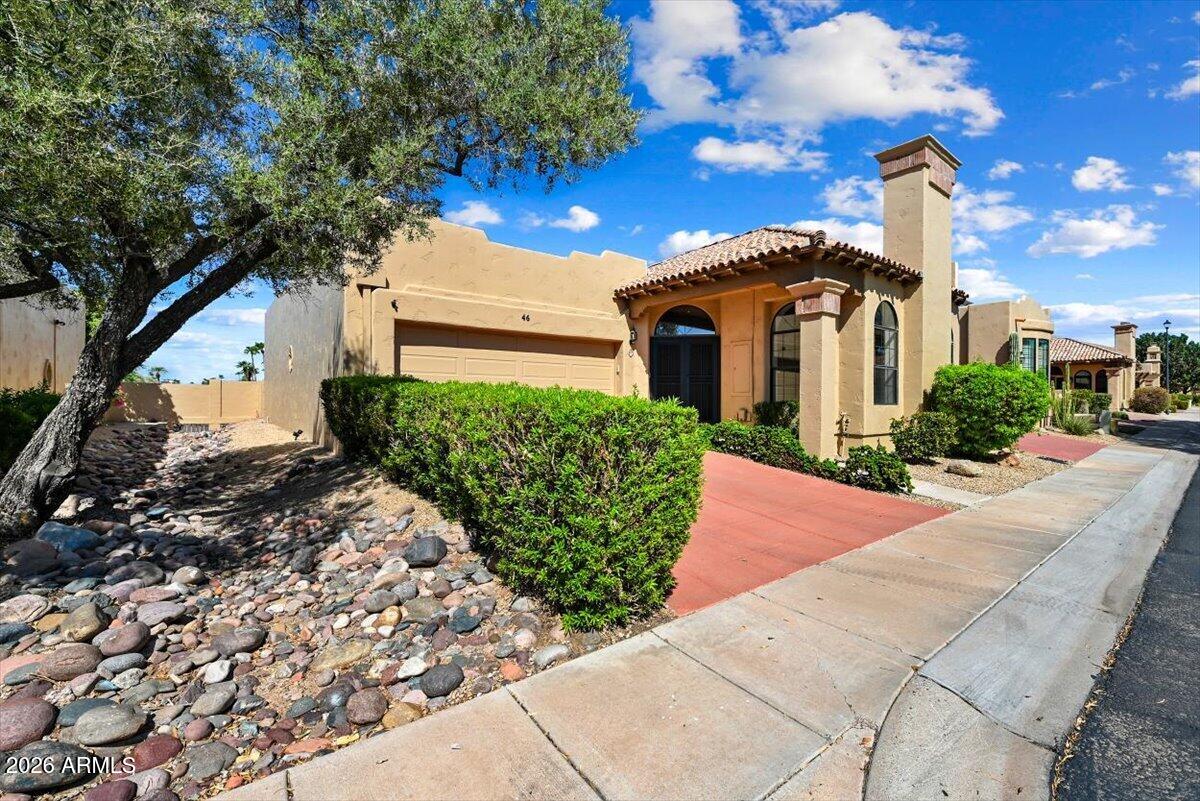 Tan stucco home with a red tile roof, attached garage, tall chimney, and rock landscaping.
