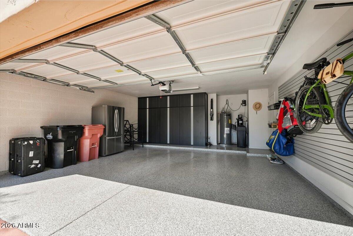 Spacious garage with a speckled floor, dark storage cabinets, refrigerator, and wall-mounted bicycles.
