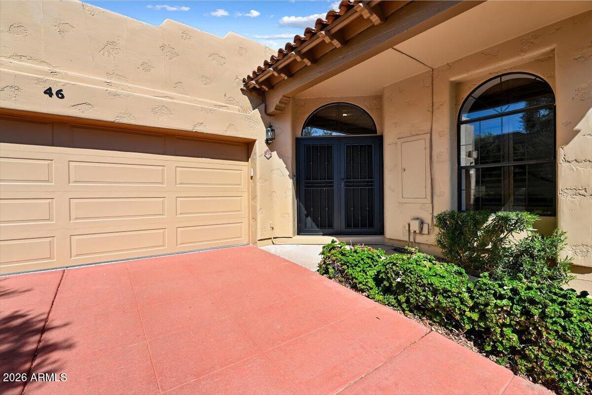 Home exterior with a two-car garage, arched entry, and reddish concrete driveway.