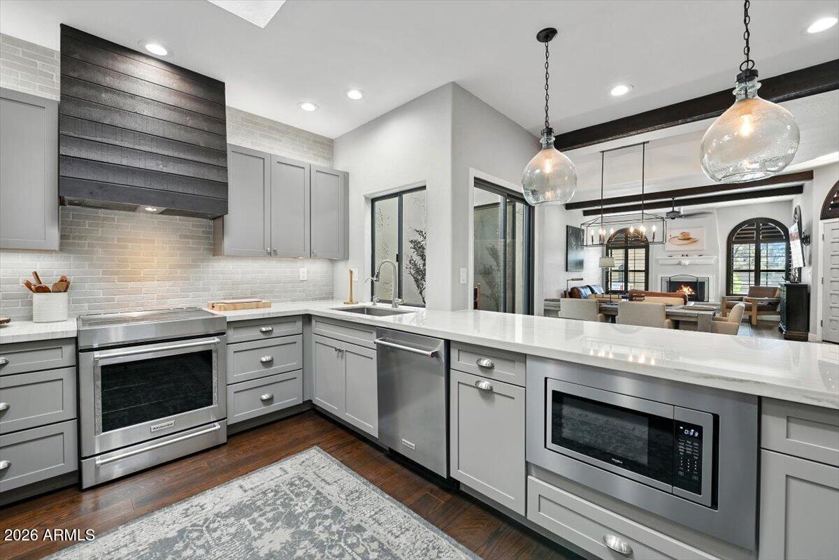 Kitchen with gray cabinets, white counters, stainless steel appliances, and an island opening to the living room.