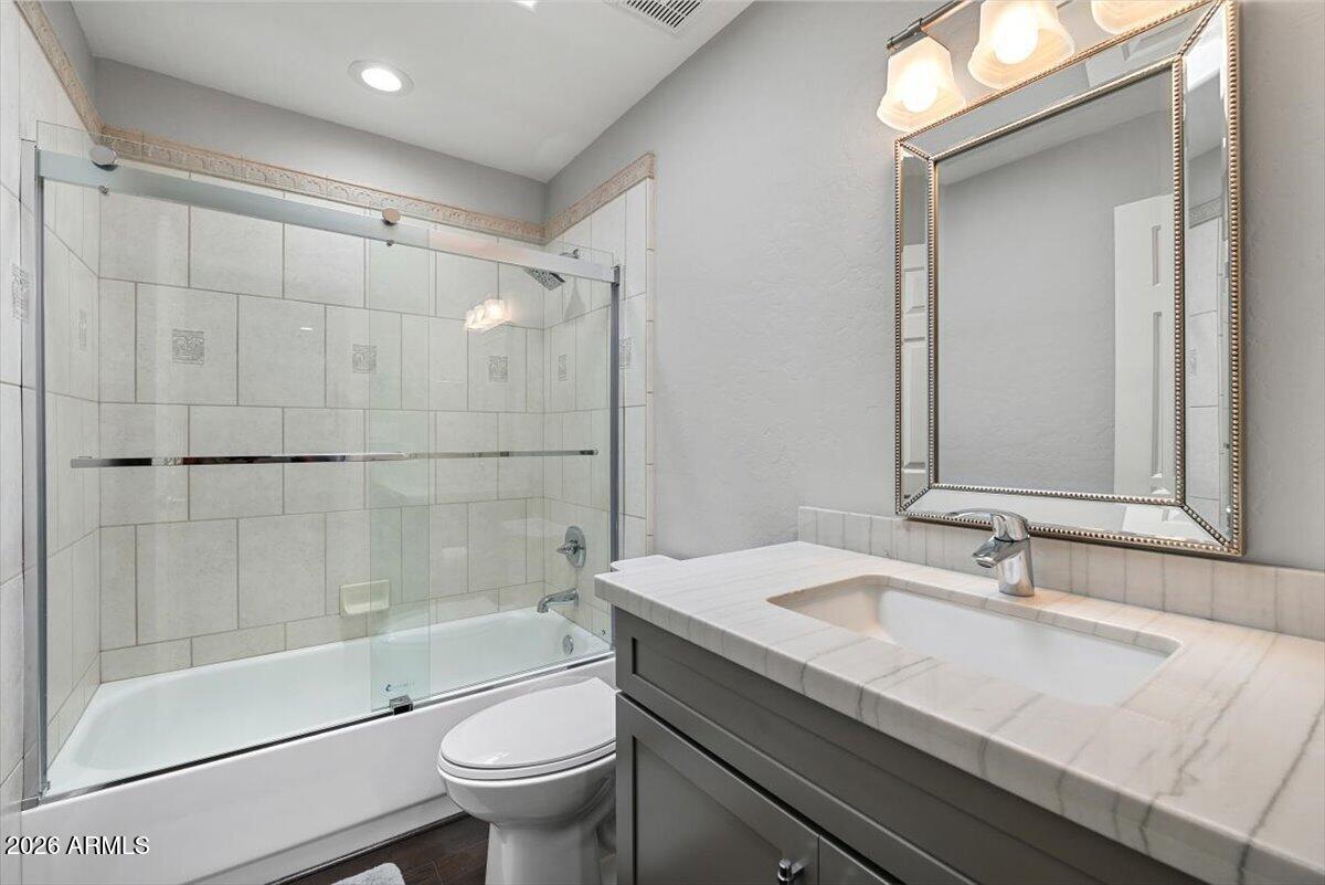 Bathroom with glass-enclosed tub and shower, tiled vanity, gray cabinetry, and framed mirror.