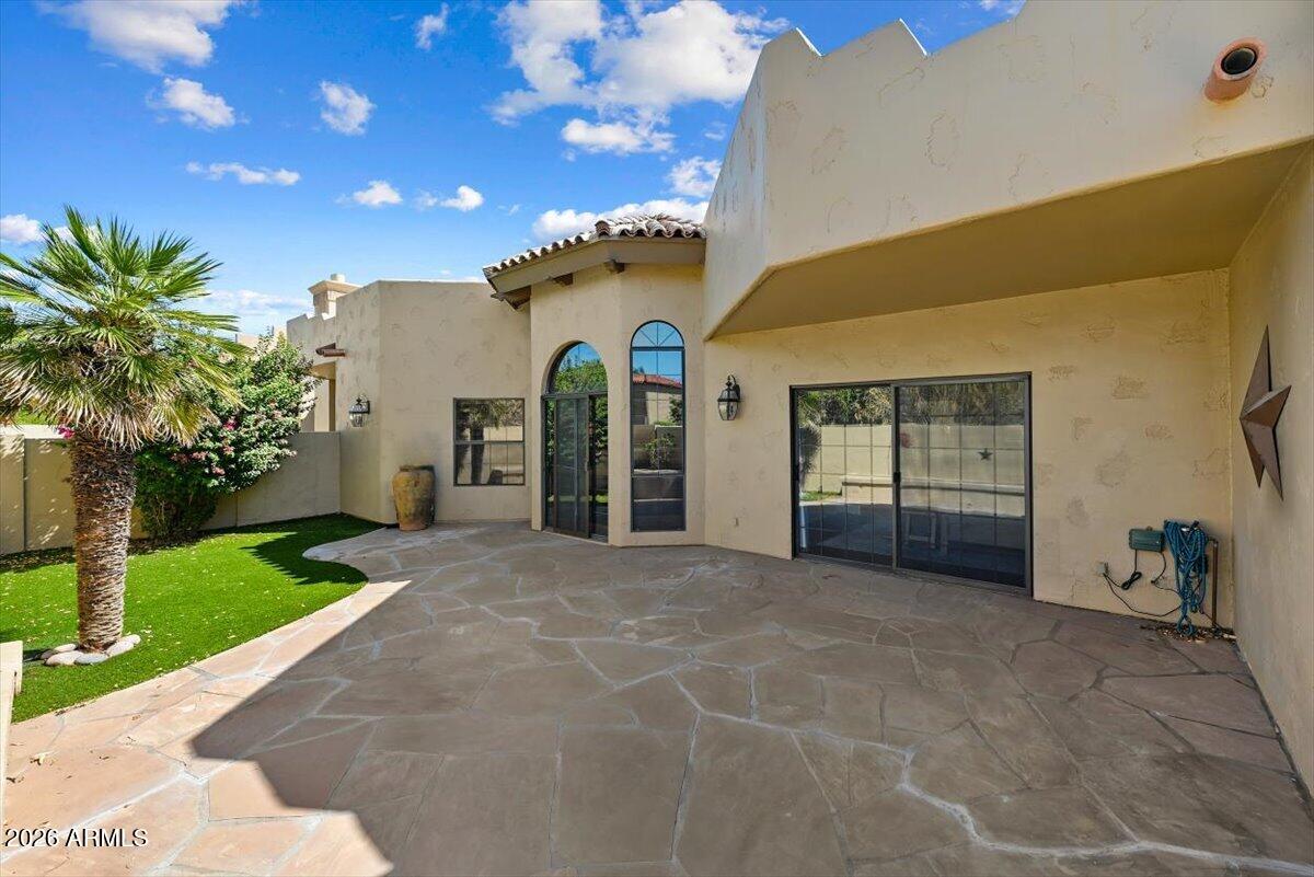 Home exterior with a broad flagstone patio, arched windows, and a palm-lined lawn.