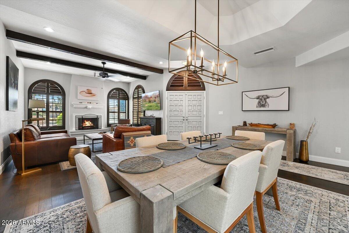 Open-plan living and dining room with arched windows, exposed beams, and a fireplace.