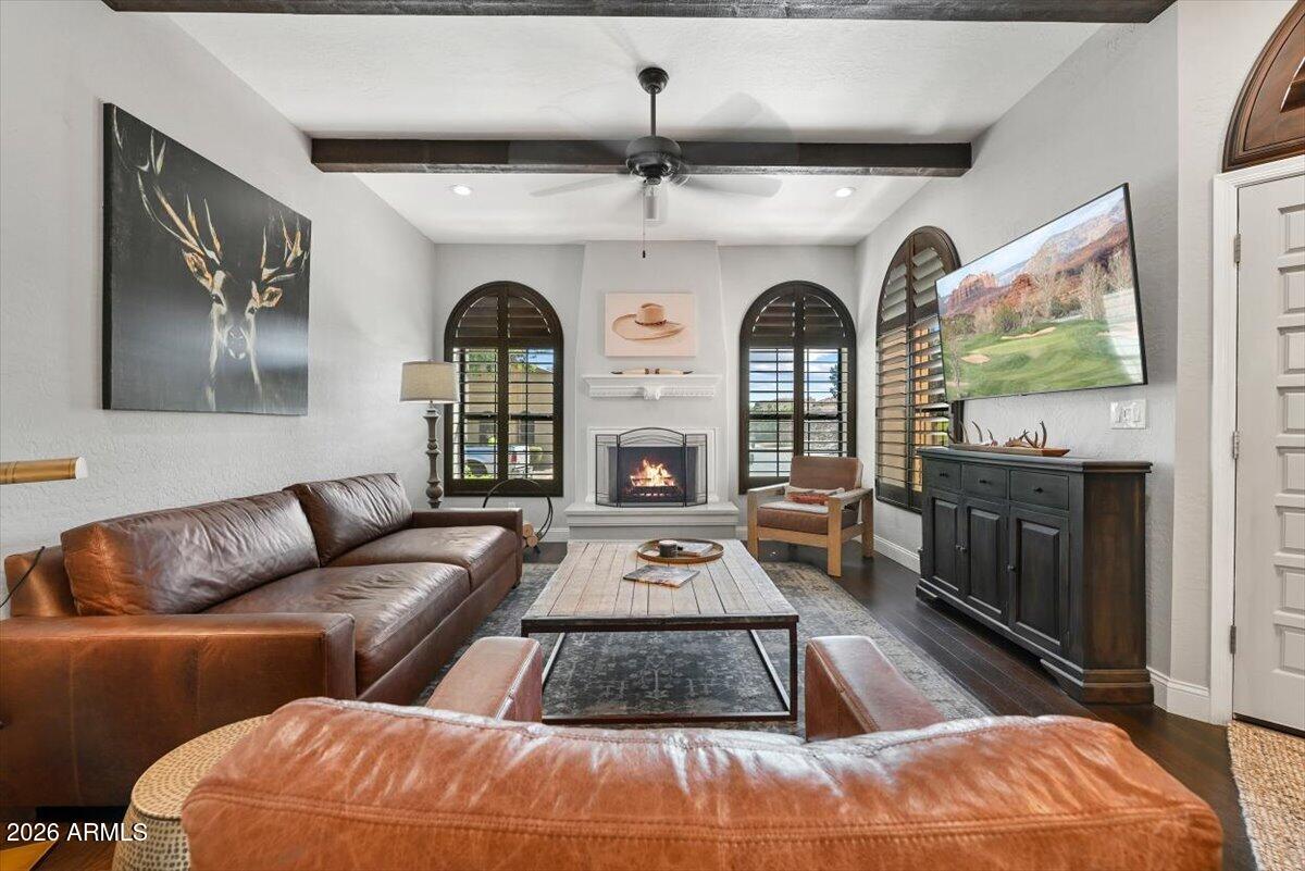 Furnished living room with leather sofas, arched shuttered windows, and a lit fireplace.