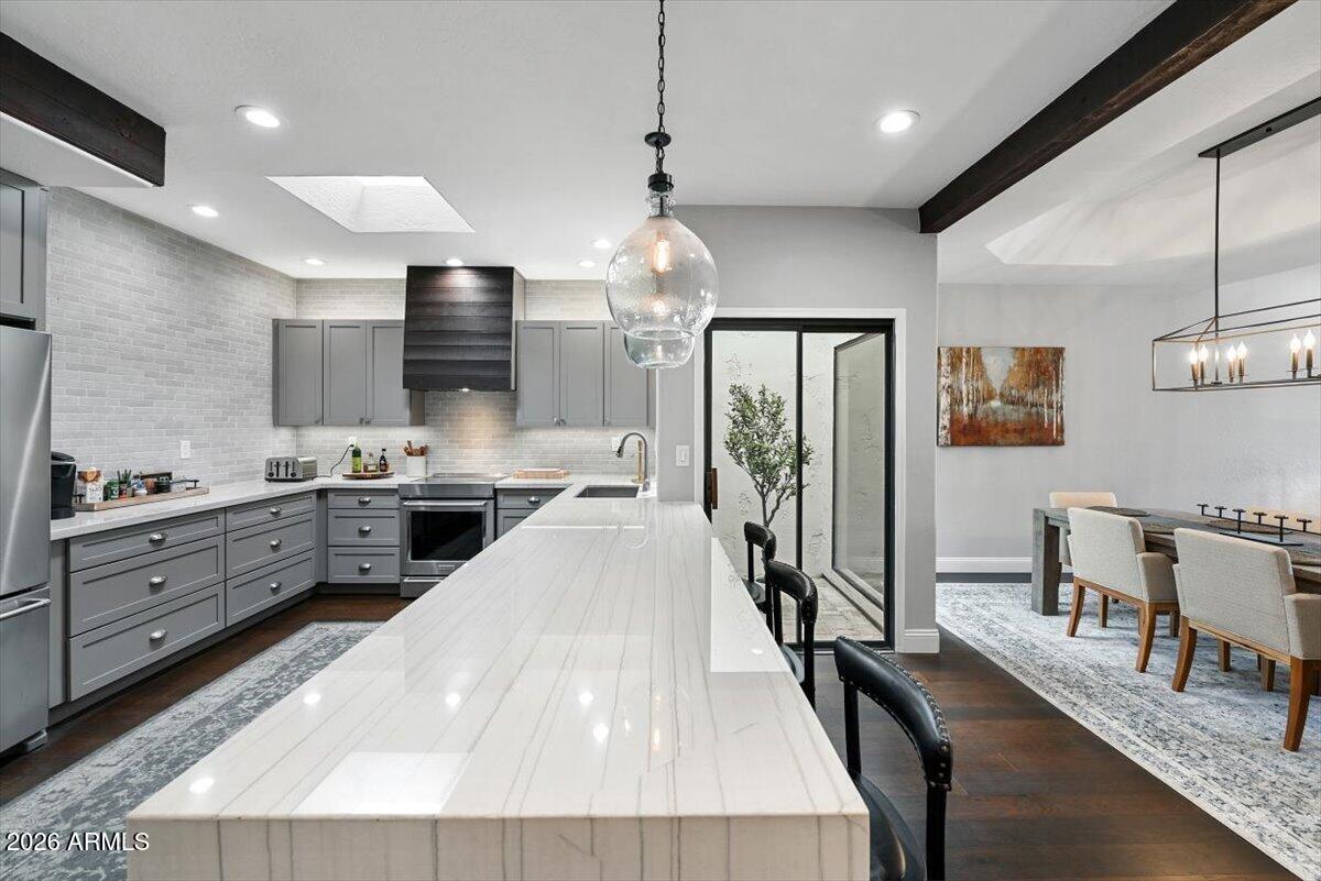 Kitchen with a long white island, gray cabinets, and an adjoining dining area.