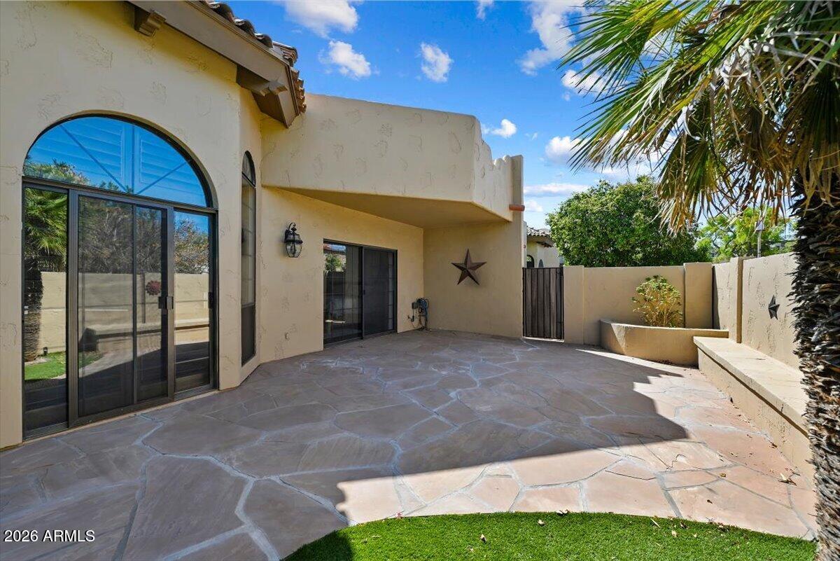 Private stone patio beside a stucco home, with arched glass doors and palm trees.