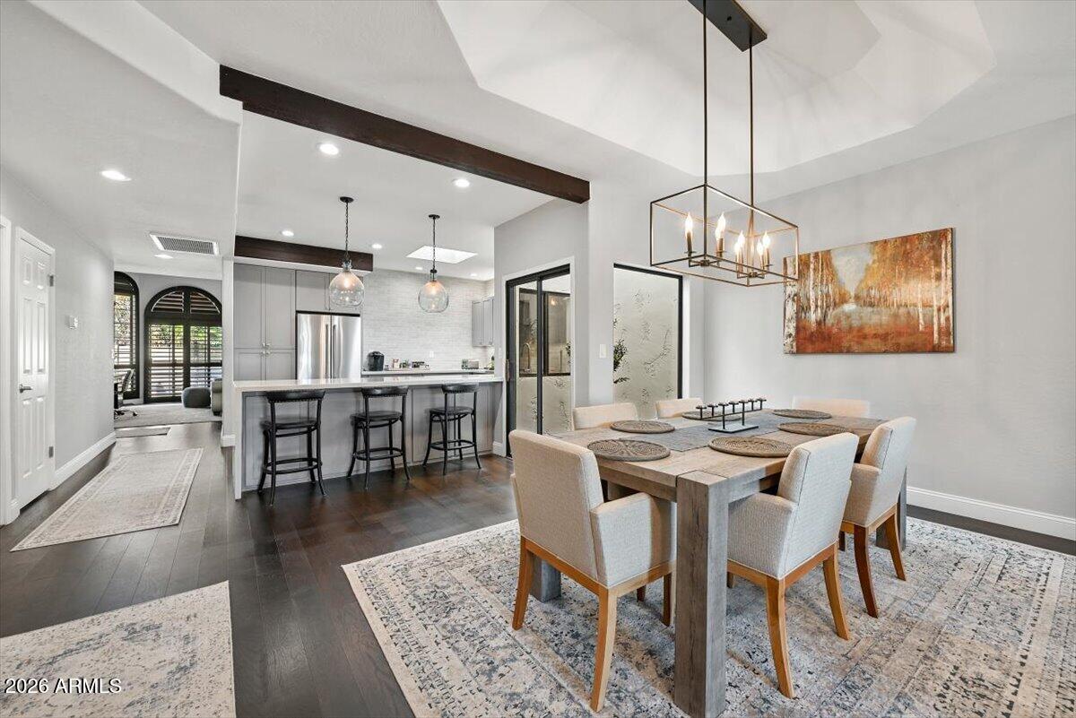 Open-plan dining room and kitchen with a wood table, island seating, gray cabinetry, and pendant lights.