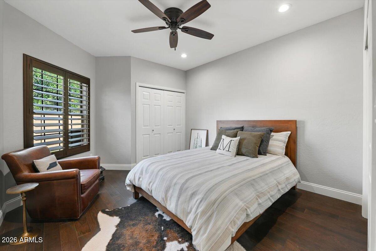 Bedroom with striped bedding, a leather armchair, plantation shutters, and dark hardwood floors.