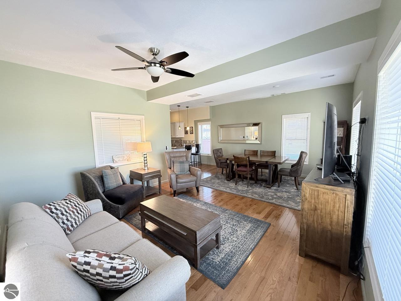 Open-plan living and dining room with pale green walls, hardwood floors, and large windows.