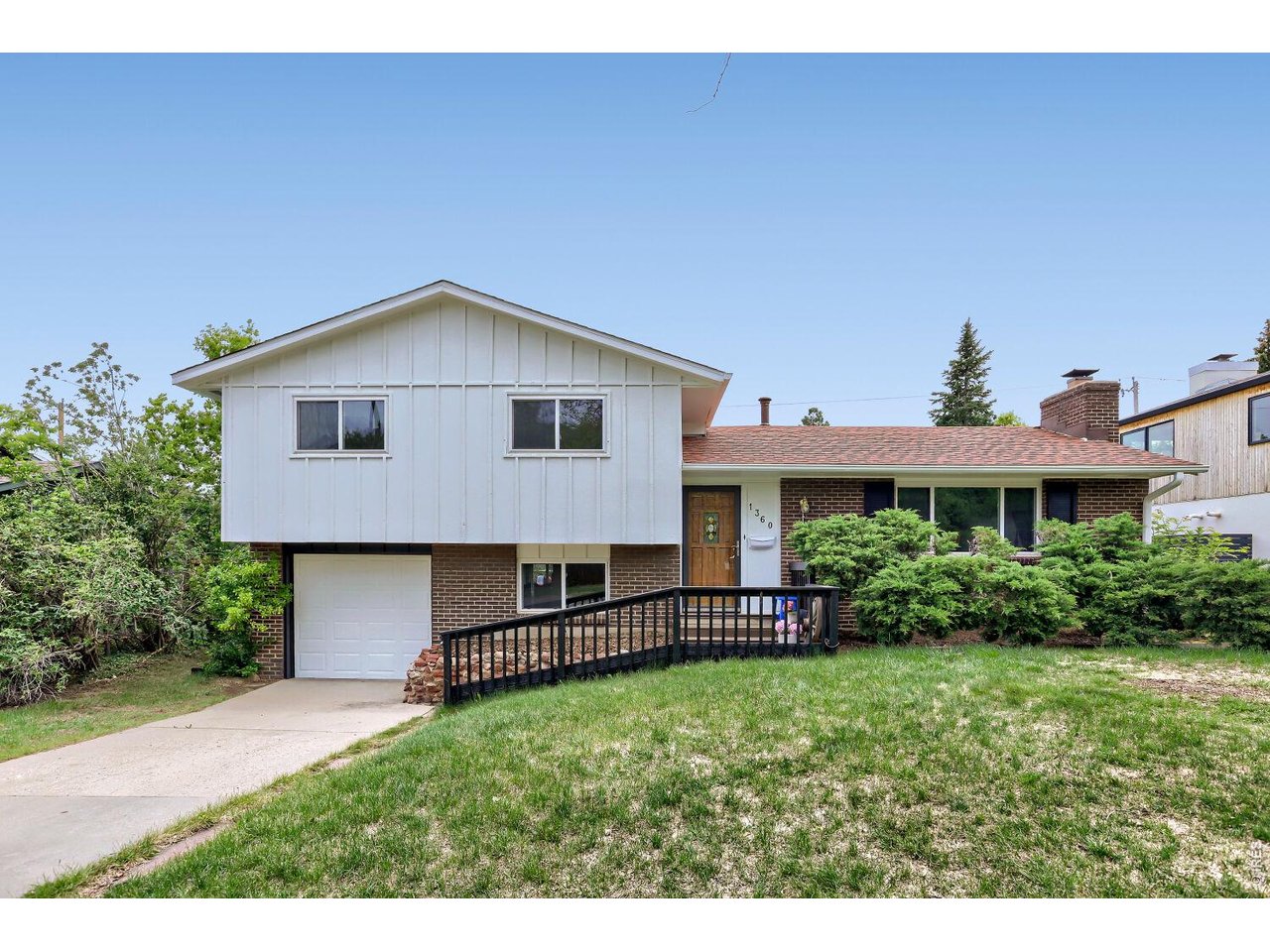 Split-level home with white siding, brick facade, attached garage, and a black-railed walkway to the entrance.