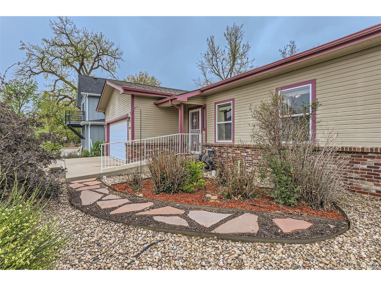Beige house with red-purple trim, brick facade, garage, and curved flagstone garden path.