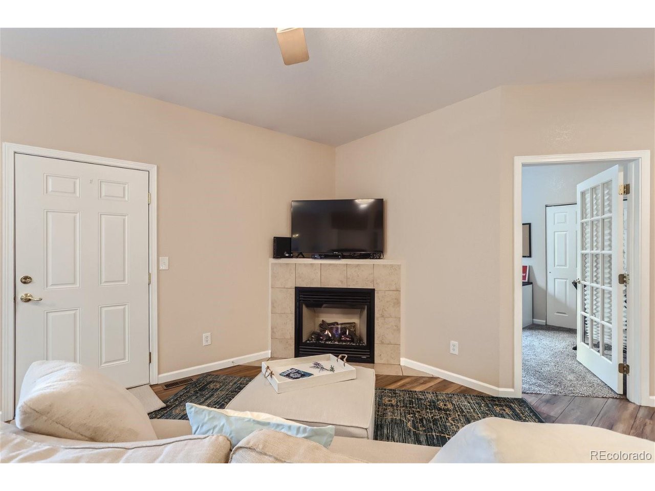 Living room with a corner gas fireplace, television, white sofas, and open French doors.