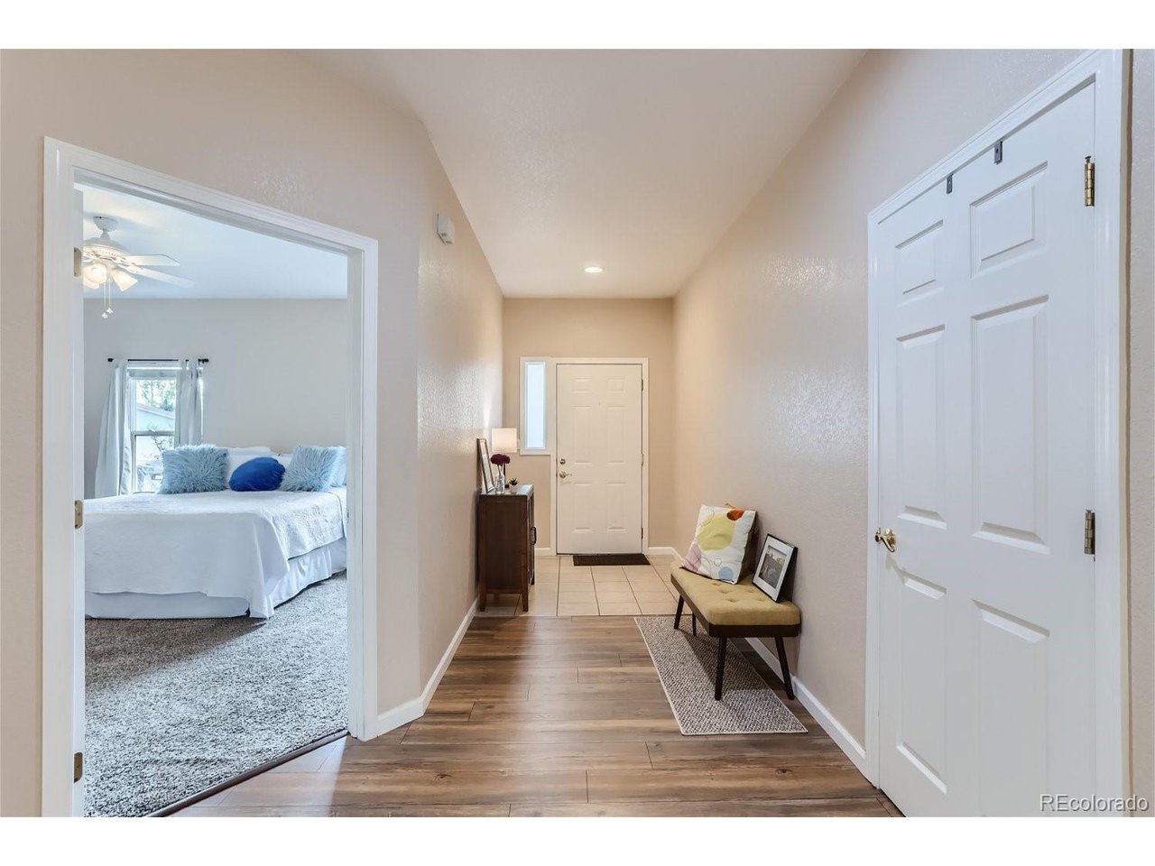 Entry hallway with wood-look flooring, a bench, and an open doorway to a bedroom.