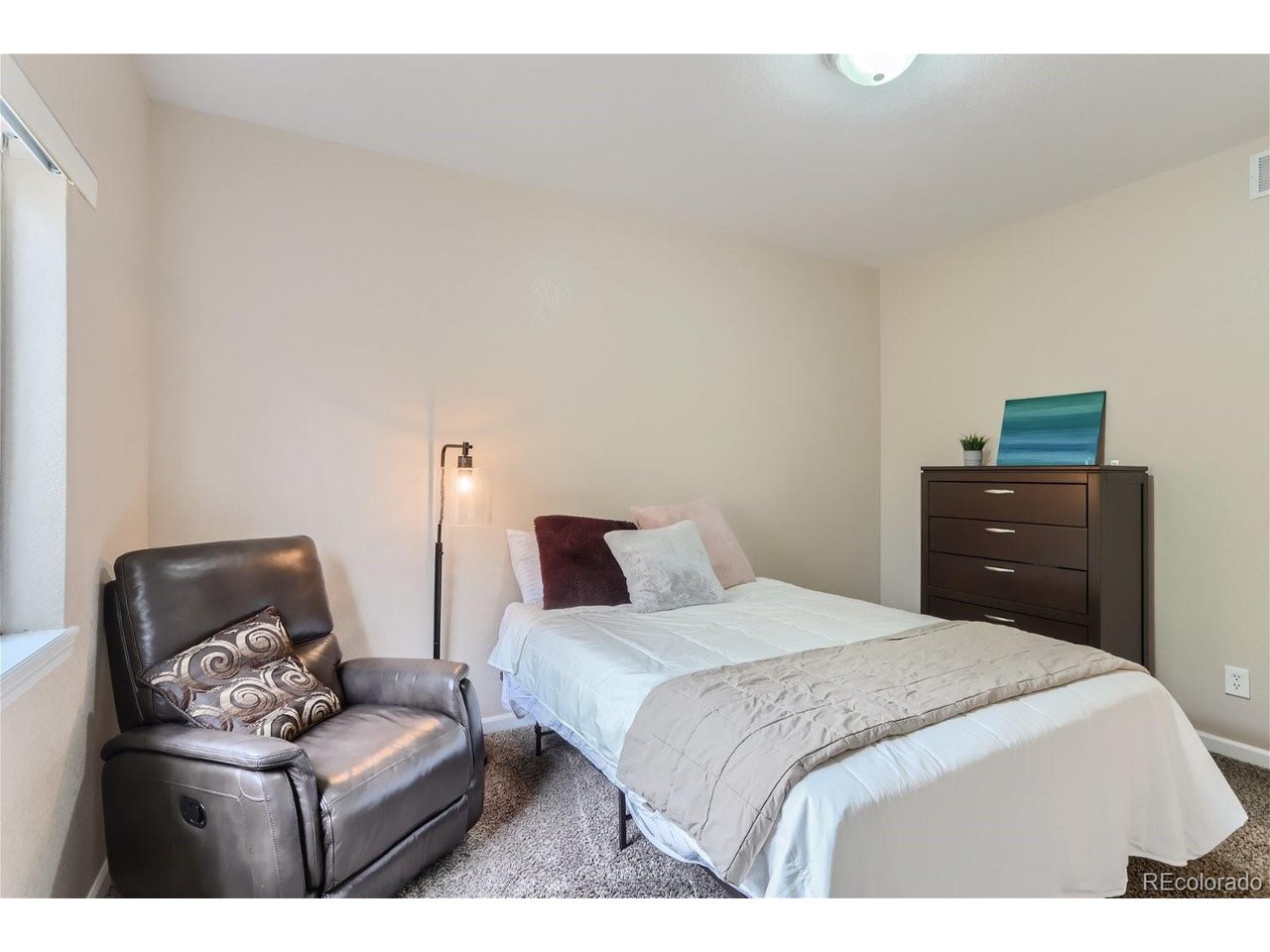 Furnished bedroom with a white bed, dark leather recliner, and dresser.