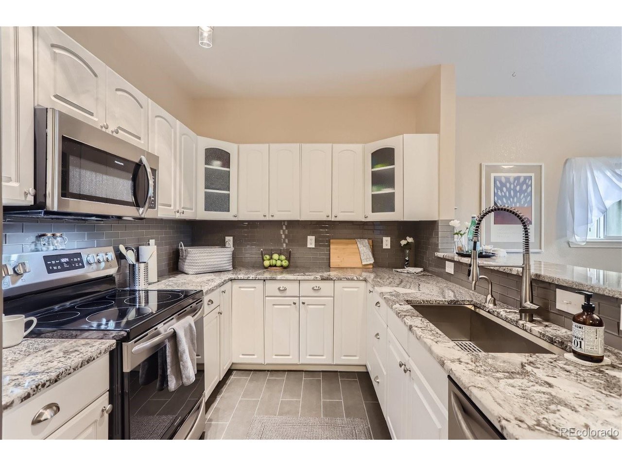 Kitchen with white cabinetry, granite counters, gray tile backsplash, and a deep double-basin sink.