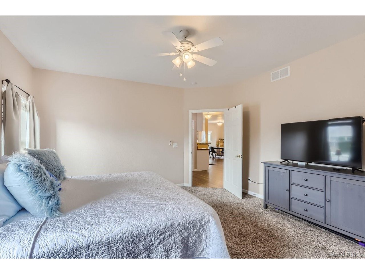 Bedroom with a white quilted bed, blue pillows, ceiling fan, and television on a dresser.