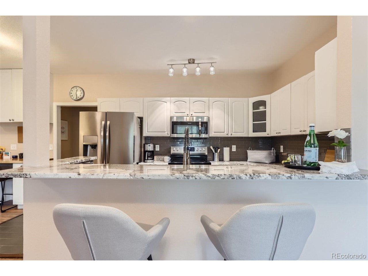 Kitchen with white cabinetry, stainless steel appliances, dark tile backsplash, and a marble-patterned island.