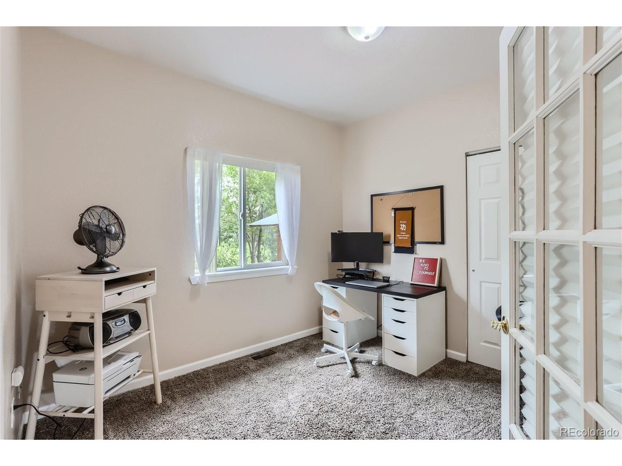 Home office with a desk and computer beside a curtained window overlooking trees.
