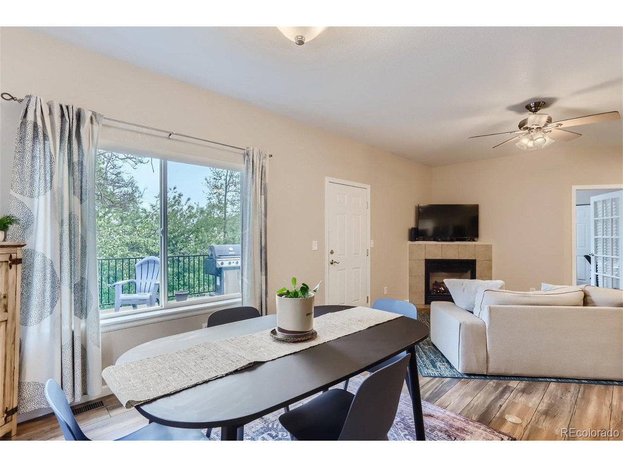 Open living and dining area with a fireplace and sliding glass door to a tree-lined deck.
