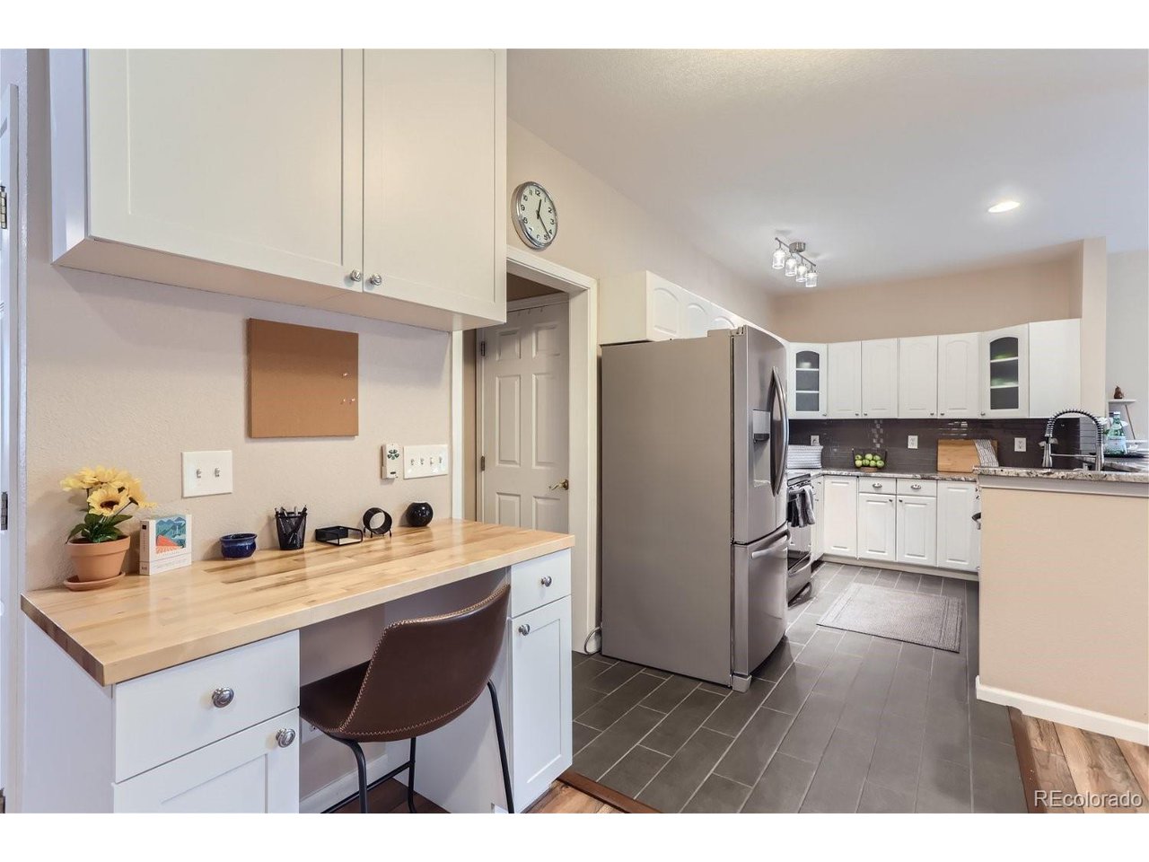 Kitchen with white cabinets, stainless-steel refrigerator, and a wood desk counter with a chair.