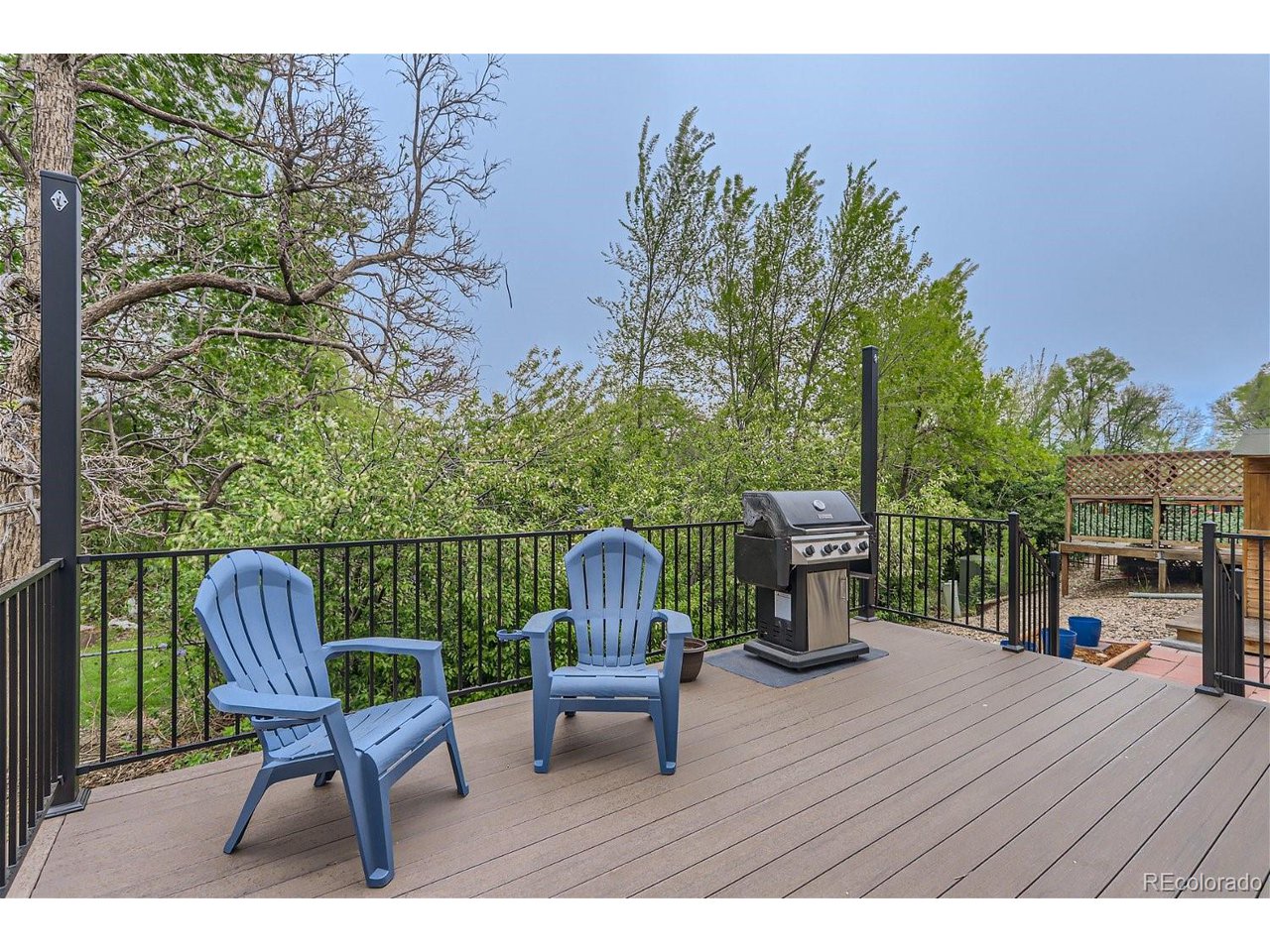 Deck with blue Adirondack chairs and a gas grill overlooking leafy trees.