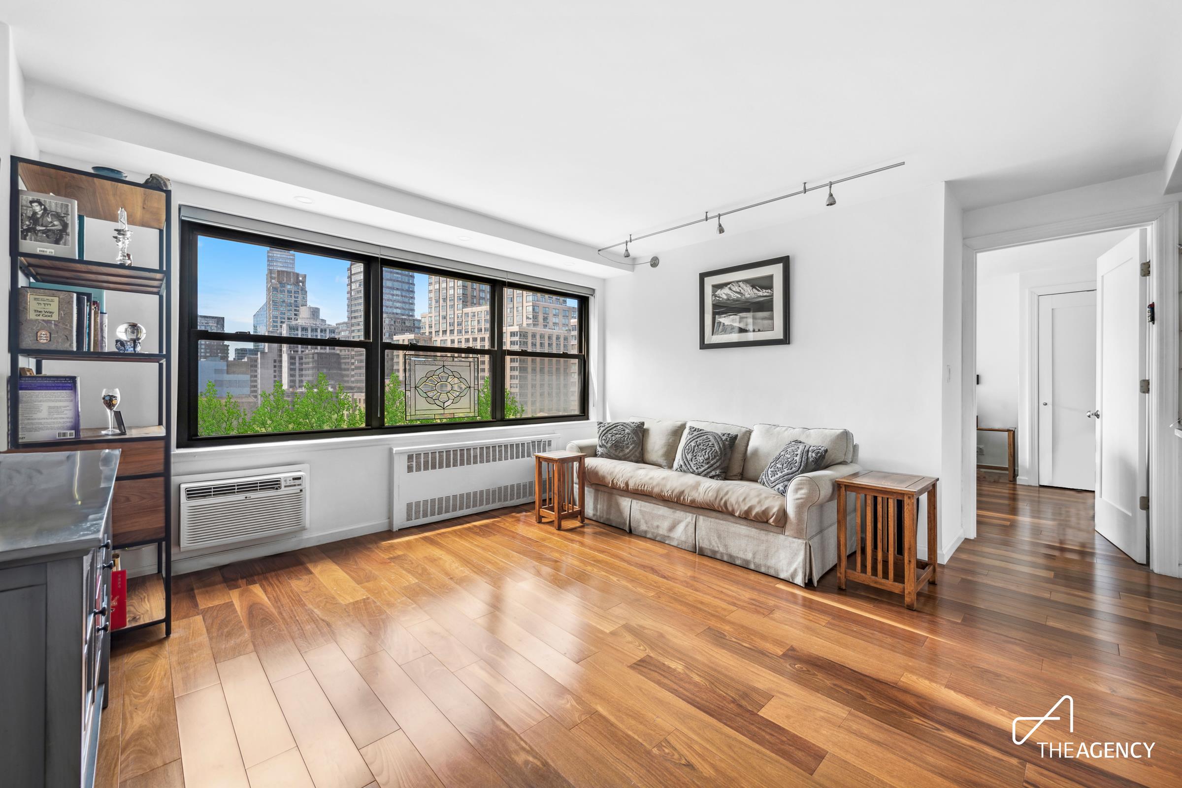 Living room with hardwood floors, a sofa, and wide windows overlooking the city skyline.