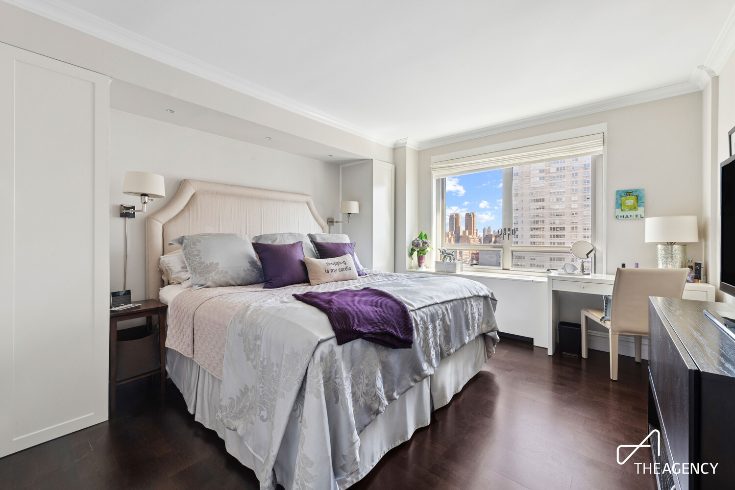 Furnished bedroom with a large bed, purple accents, and a city view through the window.
