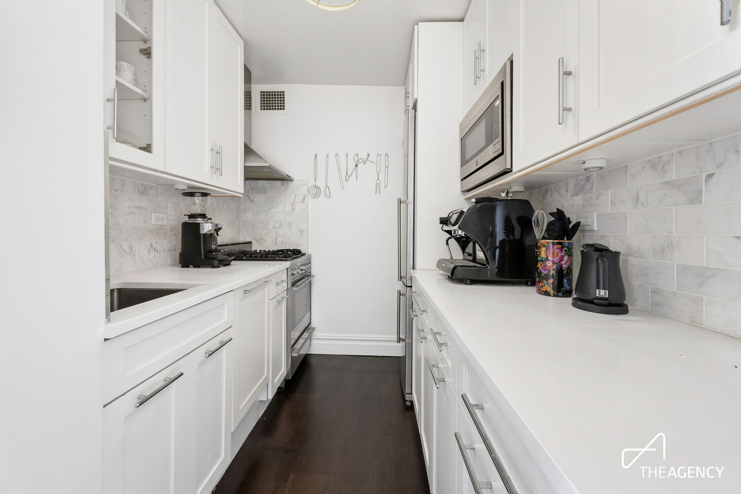 Galley kitchen with white cabinetry, marble-look backsplash, and coffee equipment on the counters.