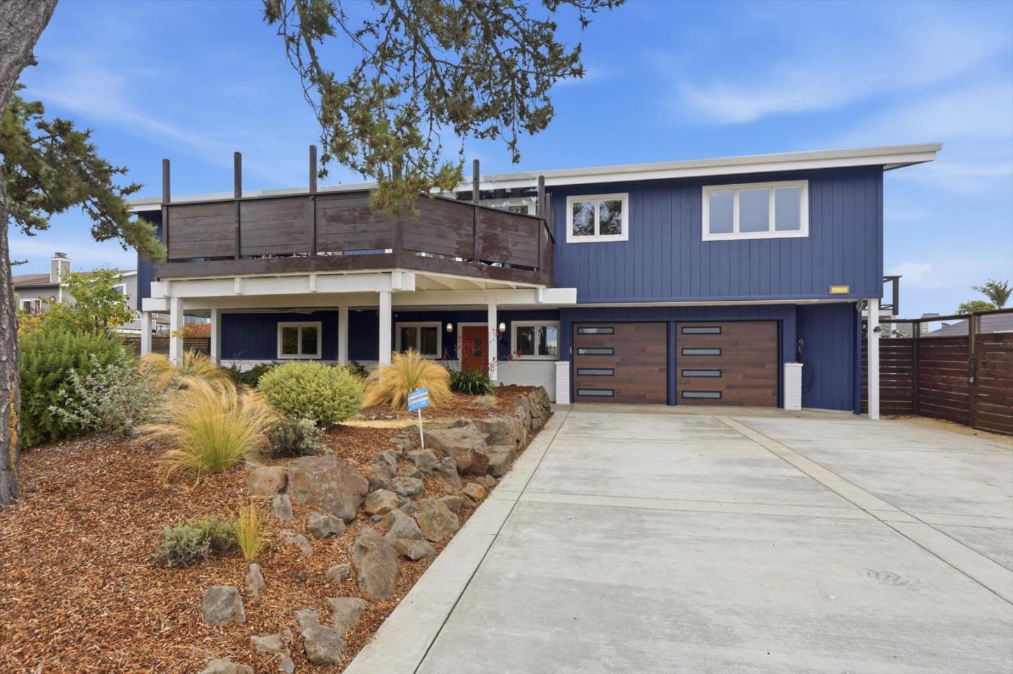 Blue two-story home with a raised deck, double garage, and landscaped front yard.
