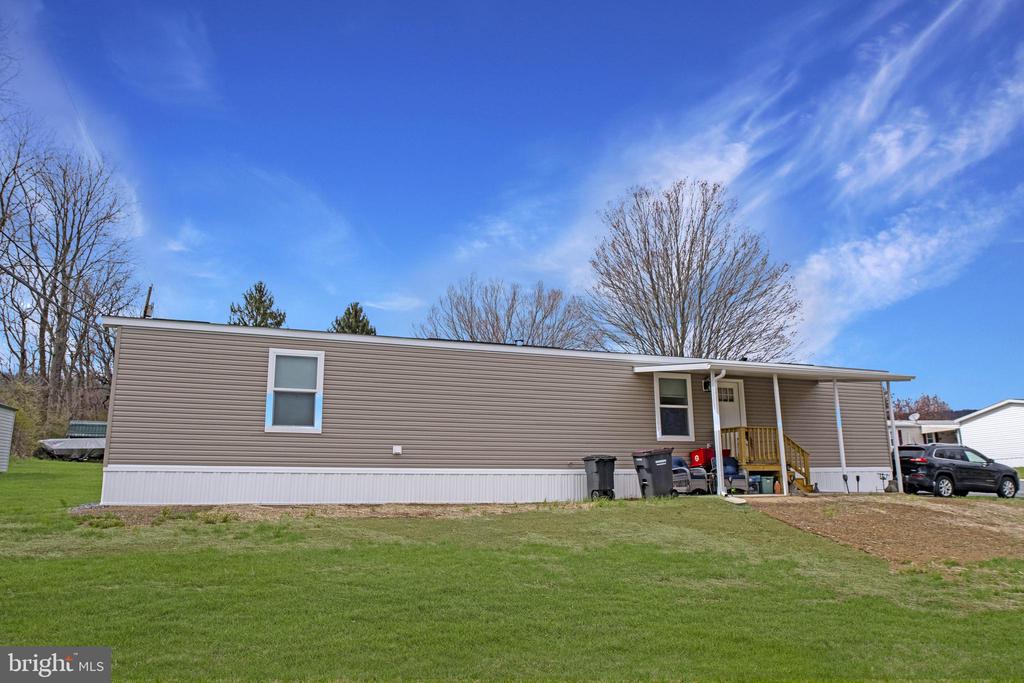 Tan manufactured home with a small covered porch and green lawn.
