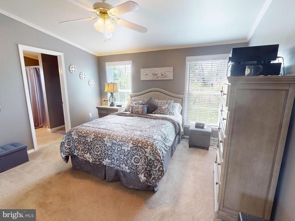 Bedroom with a patterned bedspread, upholstered headboard, and two bright windows.