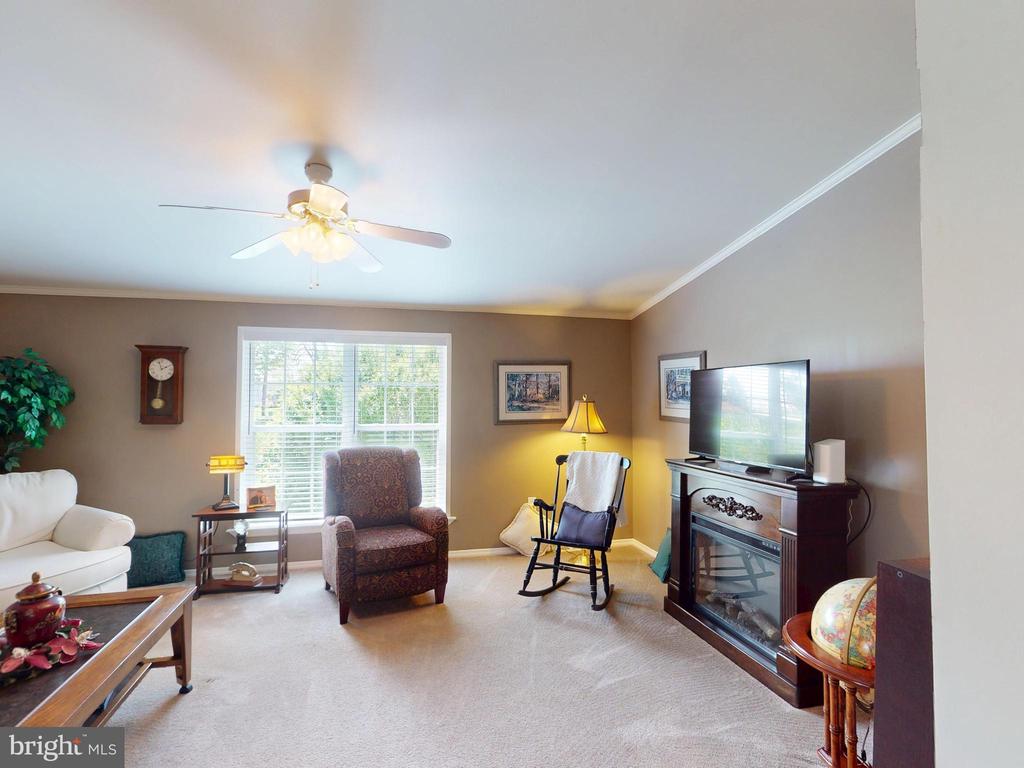 Furnished living room with a large window, rocking chair, and television above a fireplace console.