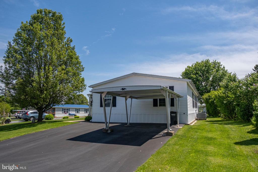 White single-story home with a metal carport, paved driveway, and mature trees.