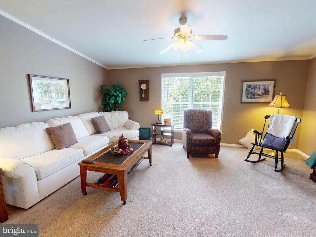Living room with a white sofa, wooden coffee table, and two armchairs around a large bright window.
