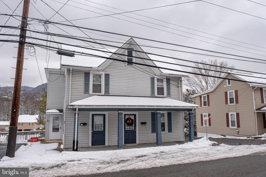 Gray two-story house with blue doors and a covered porch, seen amid snow and overhead utility wires.