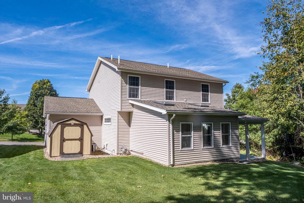 Two-story beige house with a covered porch, attached shed, and green lawn.