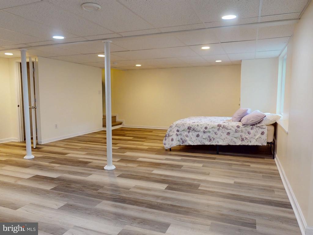Spacious bedroom with a floral-covered bed, wood-look flooring, and white support columns.