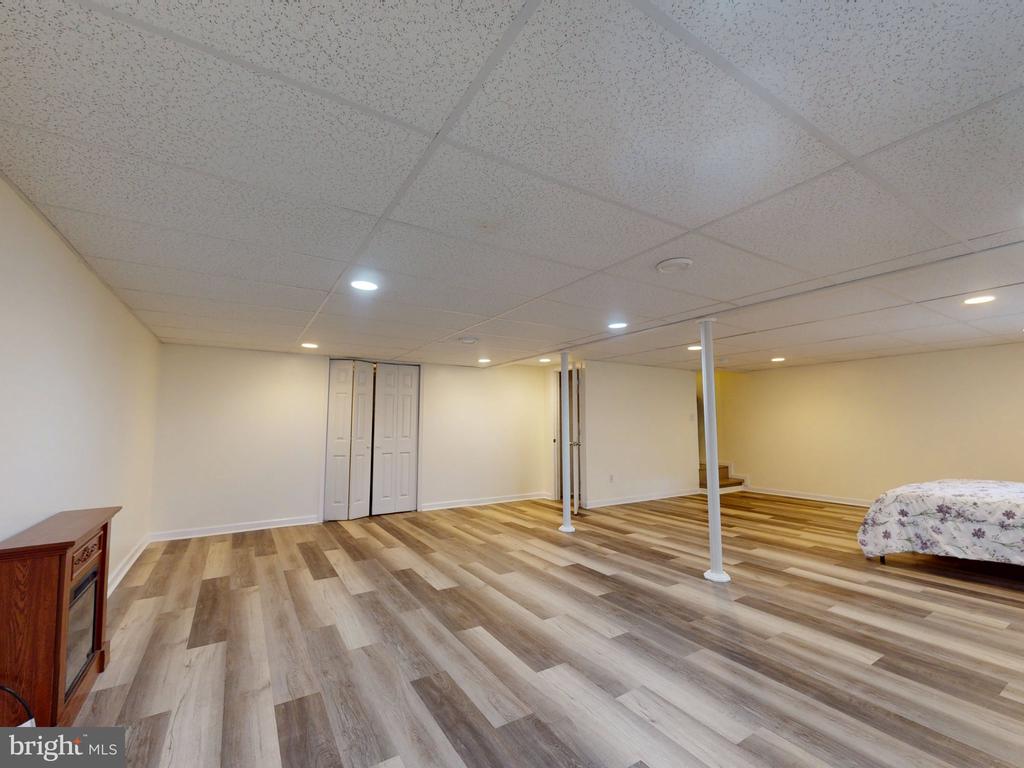 Finished basement room with wood-look flooring, recessed lights, and two support posts.