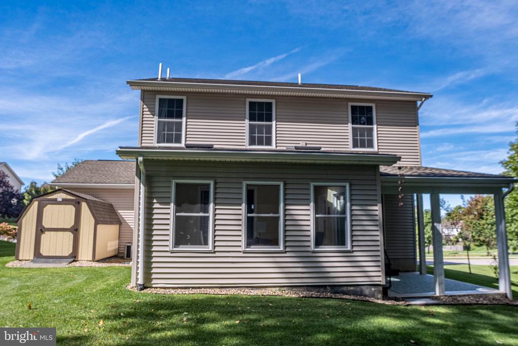 Rear exterior of a two-story gray-sided home with a covered patio and detached shed.