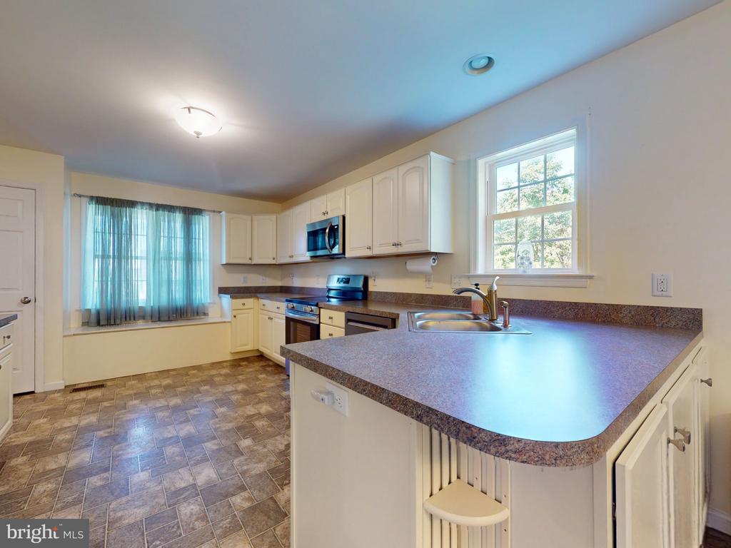 Kitchen with white cabinets, stainless appliances, and a curved breakfast bar beside two windows.
